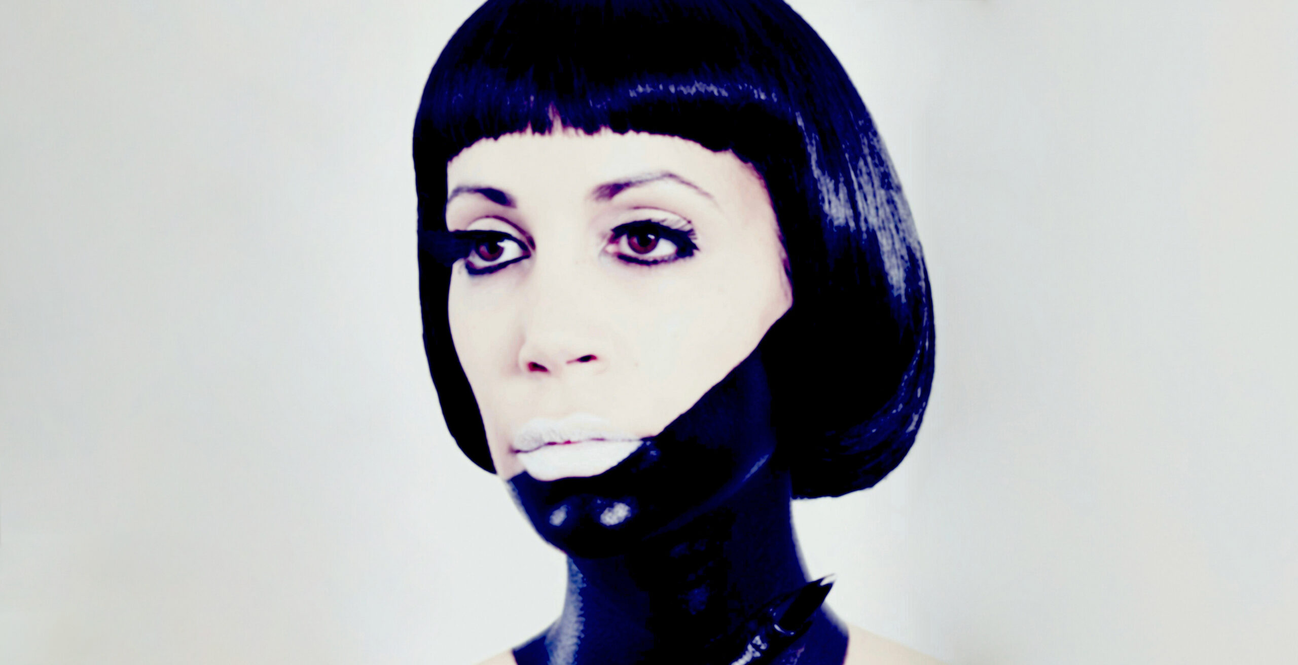 A close-up portrait of a woman wearing a jet-black bob wig and white lipstick, as well as black tribal paint covering half her face and her neck.